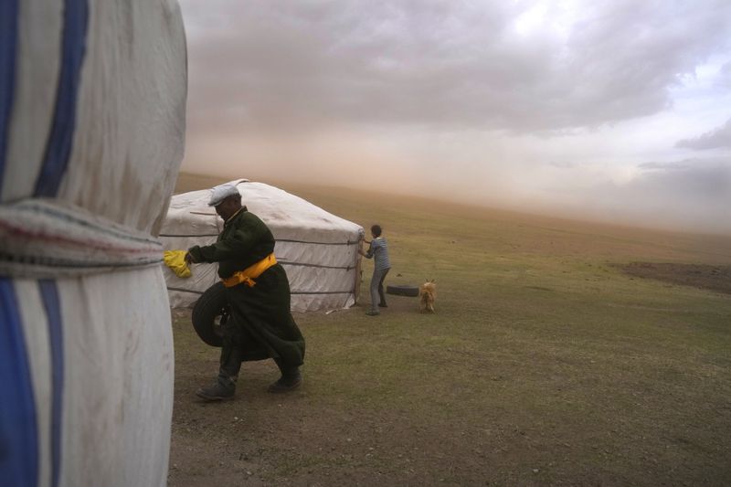 FILE- Lkhaebum, left, with his daughter-in-law, Nurmaa, check their ger, a portable, round tent insulated with sheepskin, during a sudden dust storm in the Munkh-Khaan region of the Sukhbaatar district in southeast Mongolia, Saturday, May 13, 2023. (AP Photo/Manish Swarup, File)