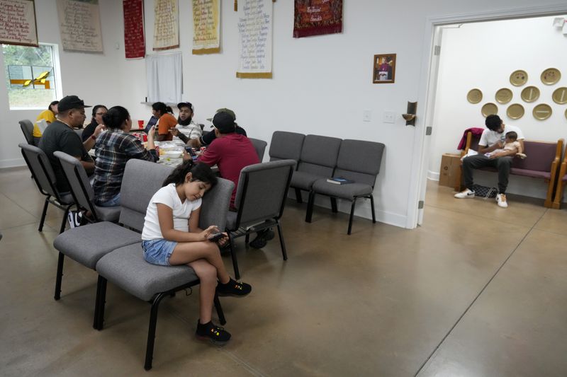 Adults gather at a table for a meal as life goes on around them inside St. Michael the Archangel Catholic church in the aftermath of Hurricane Helene Friday, Oct. 4, 2024, in Erwin, Tenn. (AP Photo/Jeff Roberson)