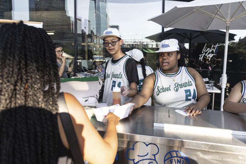 Students from Food and Finance high school serve foods during a summer block party outside the Barclays Center, Thursday, July. 11, 2024, in New York. (AP Photo/Jeenah Moon)