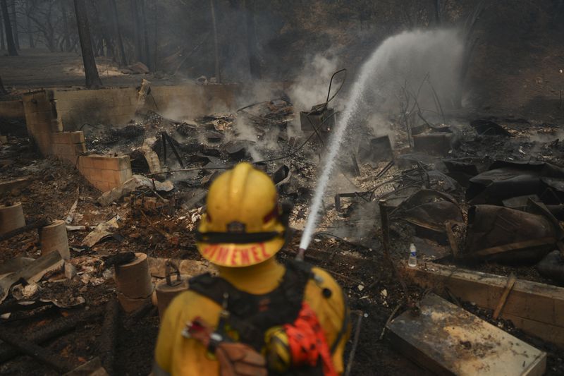 A firefighter hoses down hot spots on a fire-ravaged property while battling the Bridge Fire Wednesday, Sept. 11, 2024, in Wrightwood, Calif. (AP Photo/Eric Thayer)