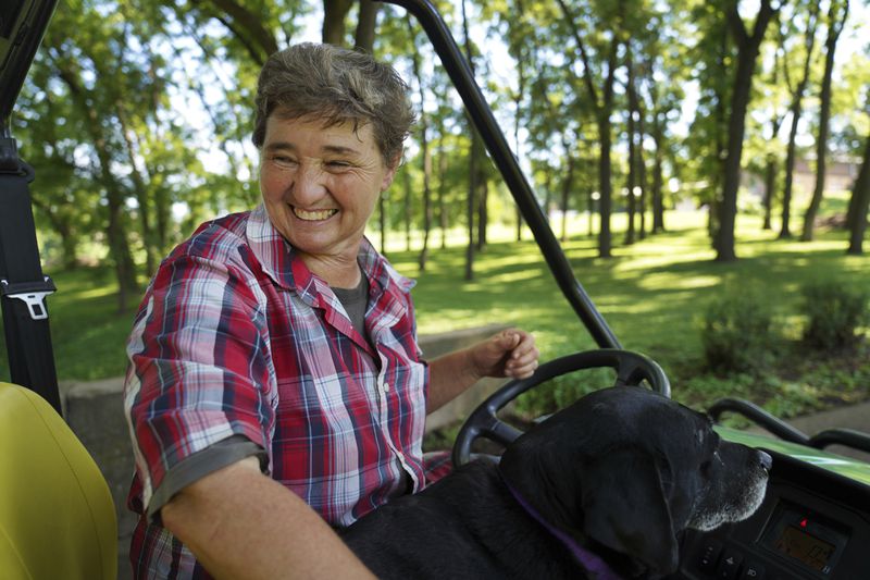 Sister Elaine Fischer rides through the Mount St. Scholastica Benedictine monastery grounds with Sophie, the community's dog, on Wednesday, July 17, 2024, in Atchison, Kansas. Fischer serves in maintenance at the monastery, caring for the buildings and grounds. (AP Photo/Jessie Wardarski)