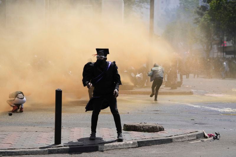 A protester wearing a graduation gown stands as Kenya police spray water canon during a protest over proposed tax hikes in a finance bill in downtown Nairobi, Kenya Tuesday, June 25, 2024. (AP Photo/Brian Inganga)
