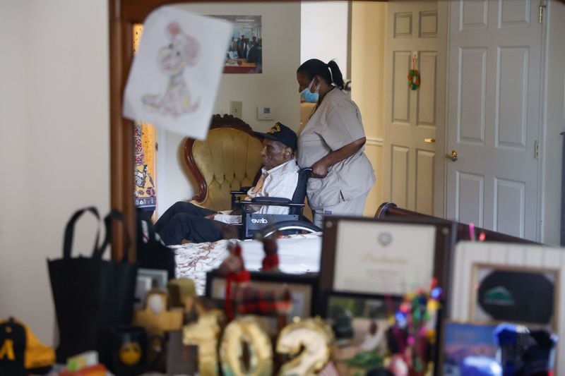 Valeria Myrick, the caregiver for William Robie, assists him in his room at Summerset Assisted Living in Atlanta on a recent morning. Robie only began using a wheelchair within the past year. His daughter credits regular socialization to her father's longevity. (Natrice Miller/AJC)