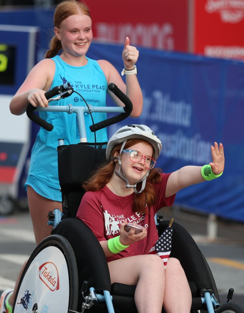 Darden Glass being pushed by sister Anna Glass crosses the finish line at the 55th running of the Atlanta Journal-Constitution Peachtree Road Race in Atlanta on Thursday, July 4, 2024.   (Jason Getz / AJC)