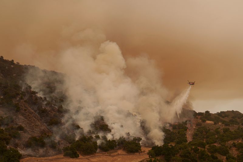 A water-dropping helicopter drops on flames from the advancing Lake Fire in Los Olivos, Calif., Saturday, July 6, 2024. (AP Photo/Eric Thayer)
