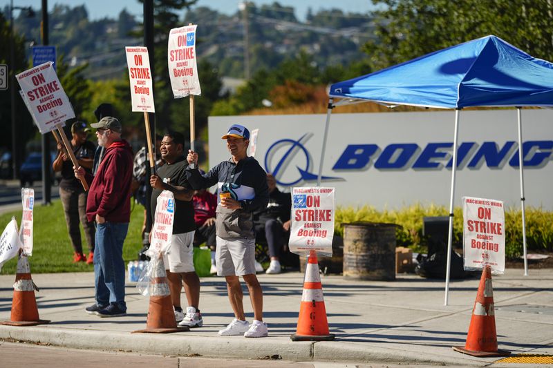 Boeing employees Cham Sin, in black, and Lou Saephanh, right center, wave signs as Boeing workers continue to strike Tuesday, Sept. 24, 2024, near the company's factory in Renton, Wash. (AP Photo/Lindsey Wasson)