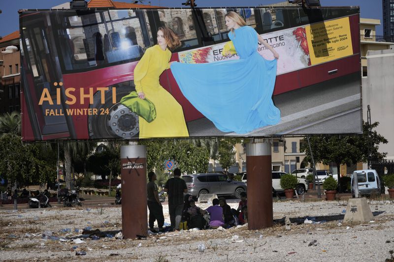 People who fled the southern suburb of Beirut amid ongoing Israeli airstrikes, take a shade under a billboard advertising fashion in downtown Beirut, Lebanon, Saturday, Sept. 28, 2024. (AP Photo/Hussein Malla)