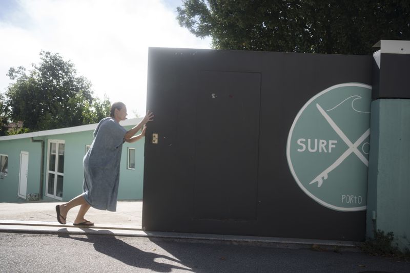 Surf Church member Marielle Louw, from South Africa, opens the garage door to her church after surfing in the suburbs of Porto, Portugal on Sunday, Aug. 18, 2024. (AP Photo/Luis Andres Henao)