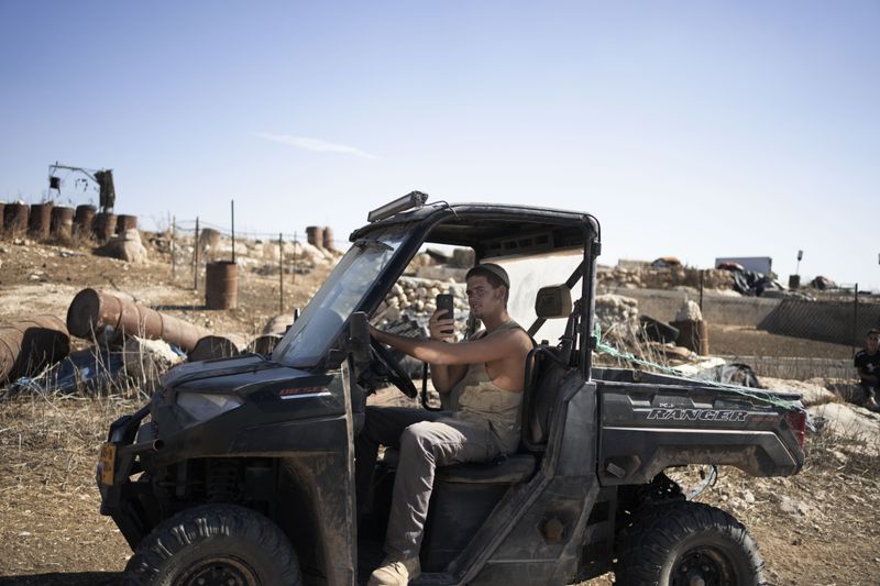 An Israeli settler films Palestinian residents and activists in the West Bank village of Khirbet Zanuta, Thursday, Aug. 29, 2024. Ten months after settlers threatened to kill them if they didn't leave their village, some Palestinian residents are finally home, under a rare court order. (AP Photo/Maya Alleruzzo)