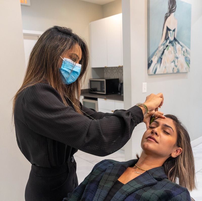 Noureen Wadhavania threads a client's brows at Beauty Brow N Beyond on Thursday, Oct 14, 2021.  Wadhvania, who is from India, says she is proud of the Indian origin of the hair removal technique. (Jenni Girtman for The Atlanta Journal-Constitution)