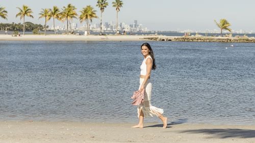 An undated handout photo of Katie Lee, author and host of the Food Network show “The Kitchen,” on the beach in Miami. Lee recommends getting away from resorts and buffets and asking locals where they like to eat. (Courtesy of Cooking Channel via The New York Times)