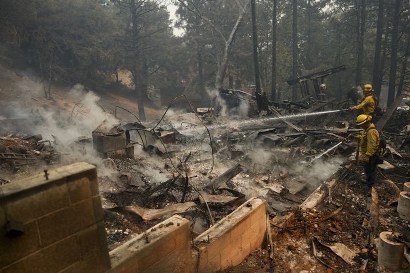 Firefighters hose down hot spots on a fire-ravaged property while battling the Bridge Fire Wednesday, Sept. 11, 2024, in Wrightwood, Calif. (AP Photo/Eric Thayer)