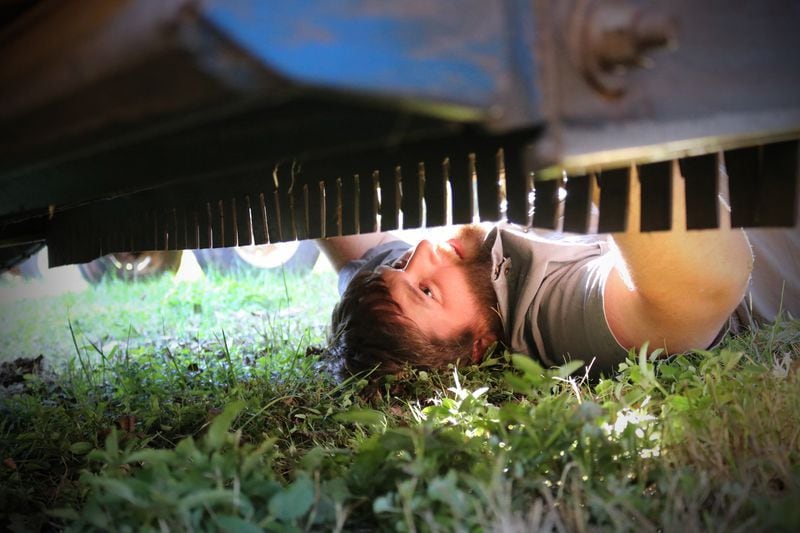 Cason Anderson works underneath a pecan harvester trying to diagnose a problem. (Eric Dusenbery for The Atlanta Journal-Constitution)