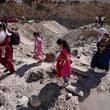 People carry their luggage as they cross into Syria on foot, through a crater caused by Israeli airstrikes aiming to block Beirut-Damascus highway at the Masnaa crossing, in the eastern Bekaa Valley, Lebanon, Saturday, Oct. 5, 2024. (AP Photo/Hassan Ammar)