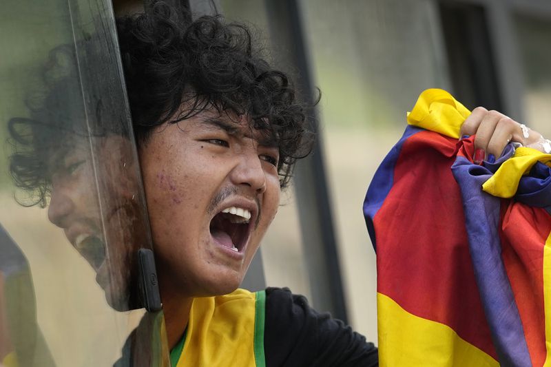 An exile Tibetan shouts slogans against the human rights situation in Tibet from a police vehicle as he is detained during a protest to coincide China marking its 75th year of Communist Party rule, outside Chinese embassy, in New Delhi, India, Tuesday, Oct. 1, 2024. (AP Photo/Manish Swarup)