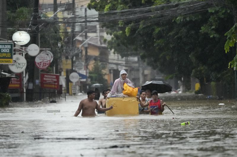 A resident rides an old refrigerator to avoid a flooded street caused by heavy rains from Tropical Storm Yagi, locally called Enteng, on Monday, Sept. 2, 2024, in Cainta, Rizal province, Philippines. (AP Photo/Aaron Favila)