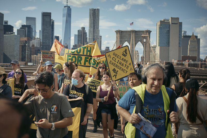 Protesters carry placards as they cross the Brooklyn Bridge during a Youth Climate Strike march to demand an end to the era of fossil fuels, Friday, Sept. 20, 2024, in New York. (AP Photo/Andres Kudacki)