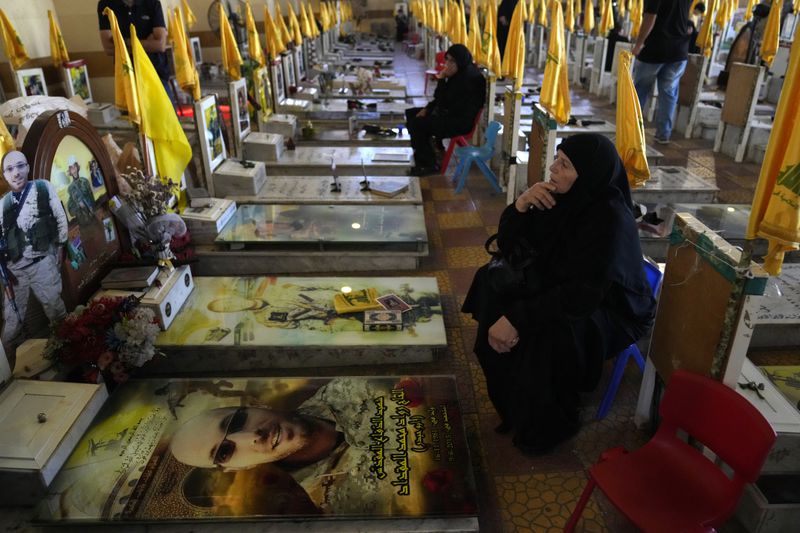 Women sit in a cemetery as they visit the graves of killed Hezbollah members in the southern suburbs of Beirut, Thursday, Sept. 19, 2024. (AP Photo/Hussein Malla)