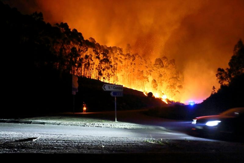 A car drives past a road closed by police as a fire burns close to it, near Sever do Vouga, a town in northern Portugal that has been surrounded by forest fires, Monday night, Sept. 16, 2024. (AP Photo/Bruno Fonseca)