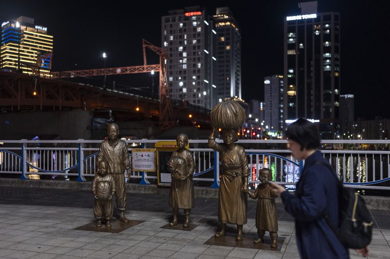 A woman walks past bronze sculptures portraying Korean War refugees in Busan, South Korea, Thursday, May 16, 2024. Busan, the only major city in the country not occupied by North Korean forces during the war, served as a refuge for those fleeing the conflict. (AP Photo/Jae C. Hong)