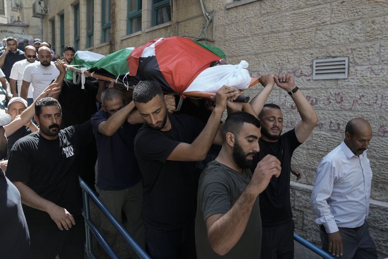 Mourners carry the body of Khalil Ziada, wrapped with a Palestinian flag, who died during an Israeli settler attack in the Wadi Rahal village, as they leave at a hospital morgue during his funeral in the West Bank city of Bethlehem, Tuesday, Aug. 26, 2024. (AP Photo/Mahmoud Illean)