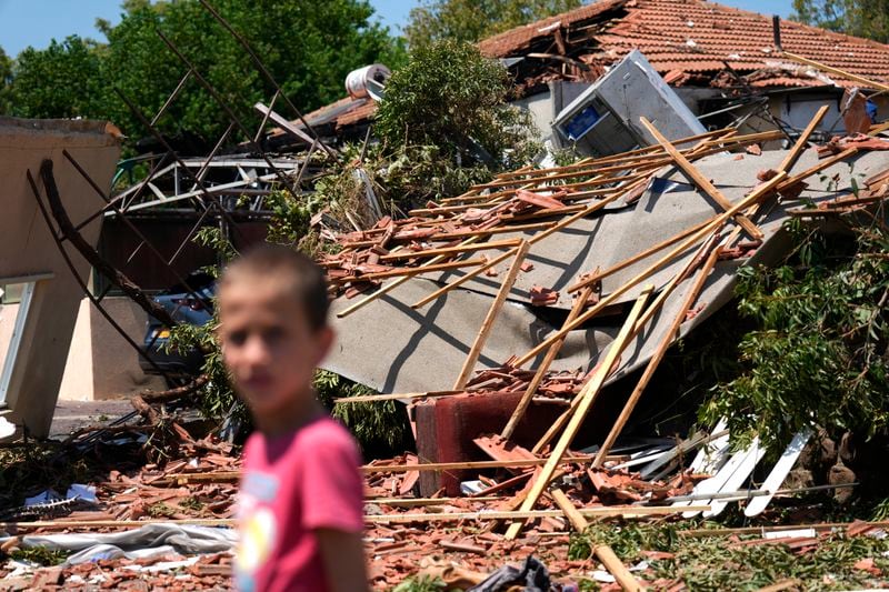 A child stands in the rubble from rocket strikes in Katzrin, in the the Israeli-annexed Golan Heights, Wednesday, Aug. 21, 2024. Lebanon's Hezbollah has launched more than 50 rockets, hitting a number of private homes in the area.(AP Photo/Ariel Schalit)