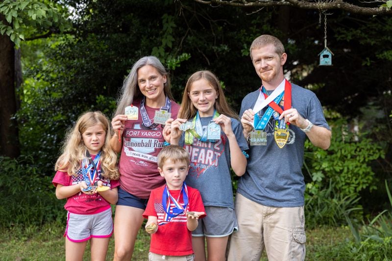 (L-R) Libby, 9; mother Ashley; James, 5; Abby, 12, and dad John Coleman pose with medals from races at their home in Decatur on Thursday, May 23, 2024.  (Arvin Temkar / AJC)