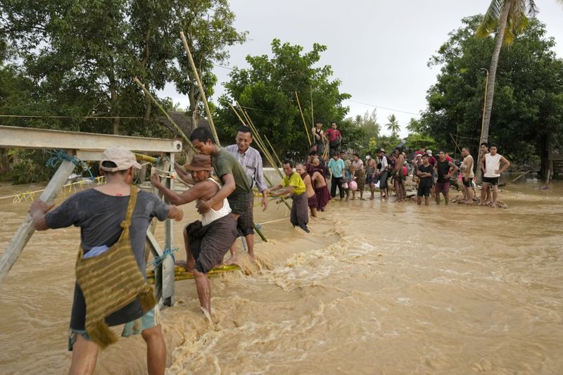 Local residents wade through flooded water at a broken bridge, in Naypyitaw, Myanmar, Tuesday, Sept. 17, 2024. (AP Photo/Aung Shine Oo)