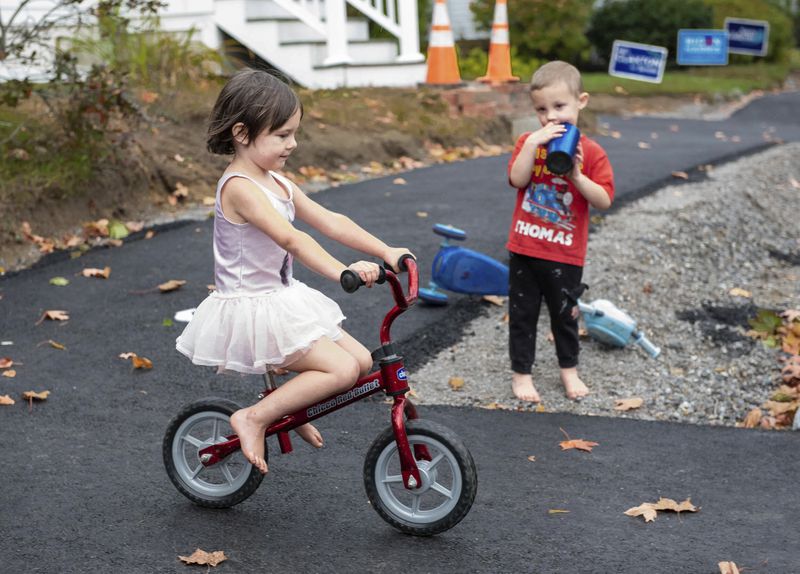 FILE - Raven Kephart, left, rides her bike down a small hill as her little brother, Teagan, looks on, Oct. 7, 2020, in Auburn, Maine. Miniature bikes with no pedals seem to be everywhere these days, and the kids riding them are getting younger and younger. Experts recommend starting with those so-called balance bikes at a younger-than-expected age, possibly even less than a year old. (Andree Kehn/Sun Journal via AP, File)