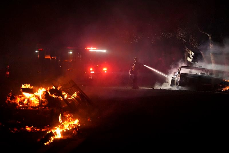 A firefighter hoses down a vehicle after the Airport Fire swept through Tuesday, Sept. 10, 2024, in El Cariso, an unincorporated community in Riverside County, Calif. (AP Photo/Eric Thayer)