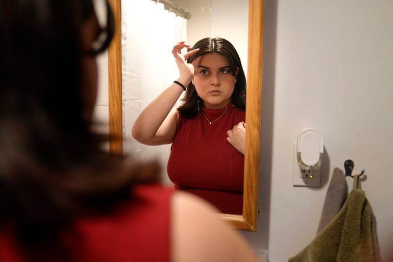 Daniella López White, of Hawaii, uses a mirror while adjusting her hair, Tuesday, May 14, 2024, at her apartment, in Boston. López White, who graduated from Emerson College in Boston this month and is on a tight budget, said TikTok influencers have helped her with tips on how to find affordable clothes at places like H&M and thrift shops. (AP Photo/Steven Senne)