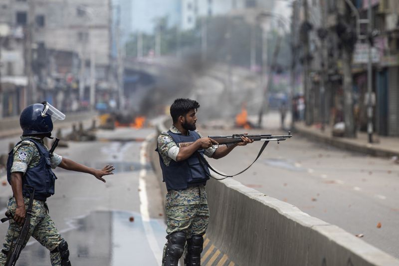 FILE - A police officer aims his weapon at protesters in Dhaka, Bangladesh, on Aug. 5, 2024, following violence during demonstrations against Prime Minister Sheikh Hasina and her government. (AP Photo/Rajib Dhar, File)