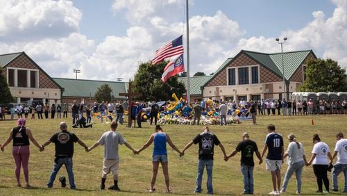 
                        Mourners hold arms in a ring around a makeshift memorial at Apalachee High School in Winder, Ga., on Saturday, Sept. 7, 2024. As residents in Winder, Ga., consoled one another, questions rose about whether more could have been done to prevent the attack in which a gunman killed two students and two teachers last week at Apalachee High School. (Christian Monterrosa/The New York Times)
                      