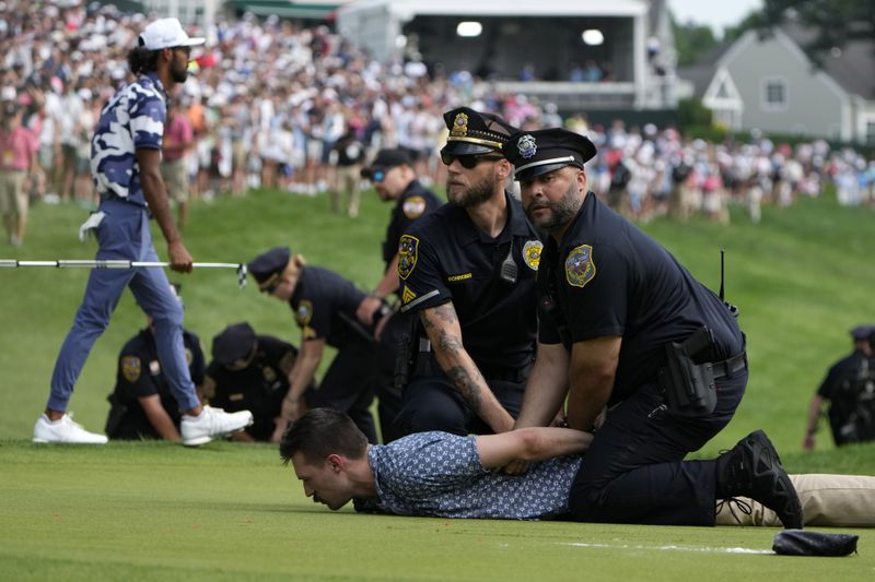 Protesters are taken into custody after they ran onto the course as Akshay Bhatia, left, walks away on the 18th hole during the final round of the Travelers Championship golf tournament at TPC River Highlands, Sunday, June 23, 2024, in Cromwell, Conn. (AP Photo/Seth Wenig)