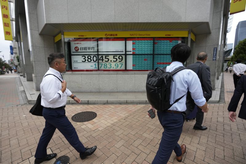 People walk by monitors showing Japan's Nikkei 225 index at a securities firm in Tokyo, Monday, Sept. 30, 2024. (AP Photo/Hiro Komae)