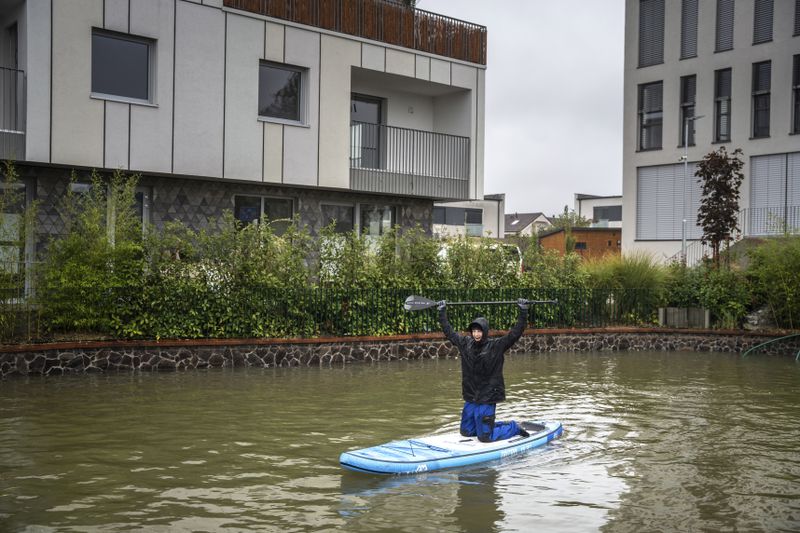 A man enjoys a ride on a padlle board during floods in Zahorska Bystrica, Slovakia, Sunday, Sept. 15, 2024. (AP Photo/Tomas Hrivnak)