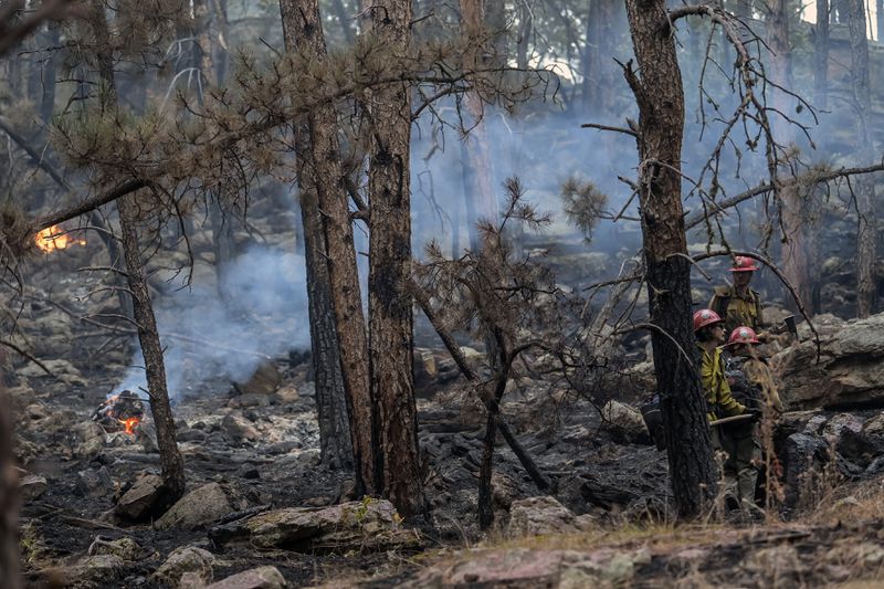 Bone piles continue to burn while hotshot crews take a moment to relax while working the First Thunder Fire on Wednesday, Sept. 4, 2024, west of Rapid City in the Black Hills, South Dakota. (Matt Gade/Rapid City Journal via AP)