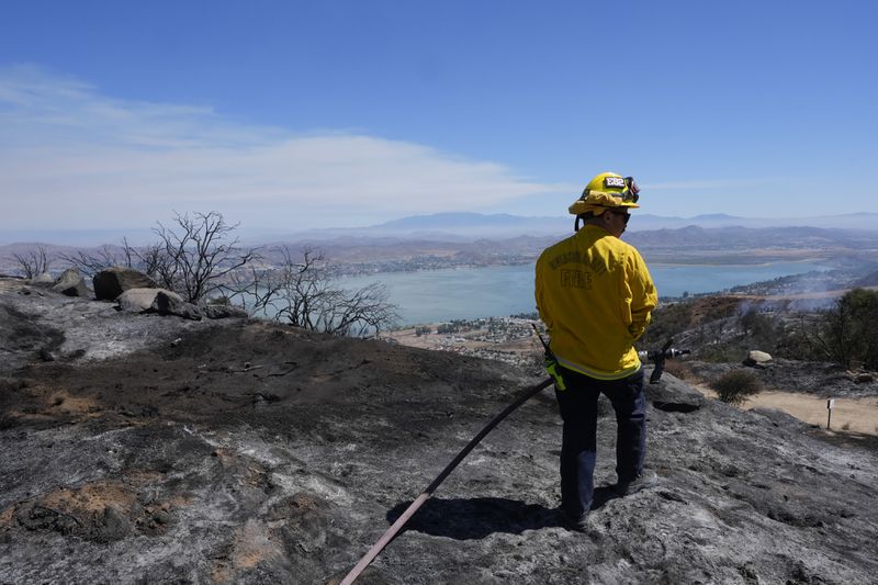 A Riverside County Fire Dept. firefighter monitors for hot spots overlooking Lake Elsinore after the Airport Fire swept through Wednesday, Sept. 11, 2024, in El Cariso Village, in unincorporated Riverside, County, Calif. (AP Photo/Gregory Bull)