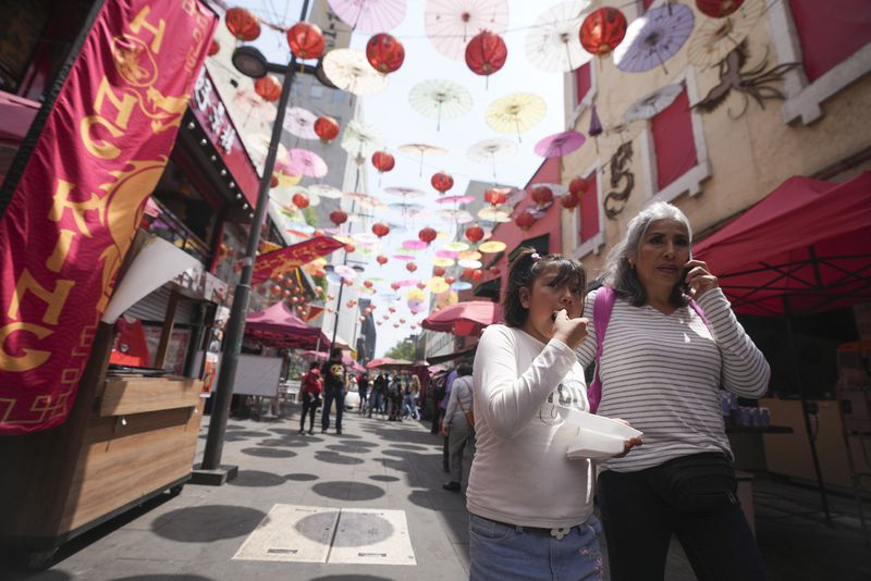 Tourists walk under colorful umbrellas and lanterns at Chinatown in Mexico City's historic center, Saturday, June 8, 2024. (AP Photo/Fernando Llano)