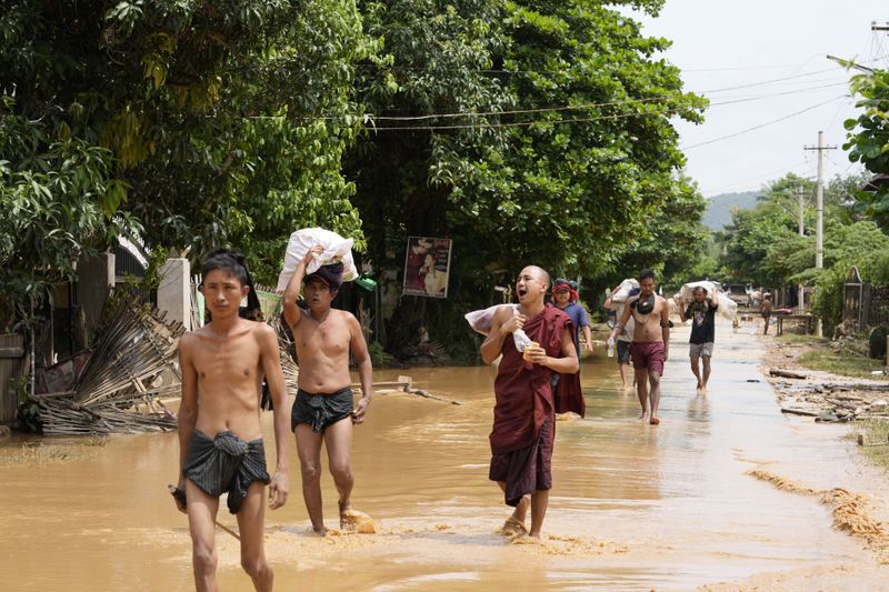 Local residents and a Buddhist monk carrying food wade through a flooded road in Naypyitaw, Myanmar, Saturday, Sept. 14, 2024. (AP Photo/Aung Shine Oo)