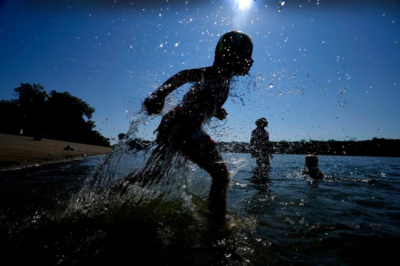 Judah Boyle, of Des Moines, Iowa, splashes water as he runs on the beach at Gray's Lake Park, Monday, Aug. 26, 2024, in Des Moines, Iowa. (AP Photo/Charlie Neibergall)