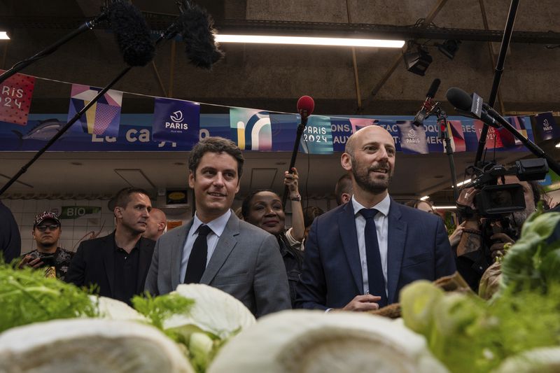 French Prime Minister Gabriel Attal, left, campaigns with local candidate for the second round of the legislative election Stanislas Guerini, Tuesday, July 2, 2024 at a market in Paris. After France's far-right National Rally surged into the lead in the first round of legislative elections, some European neighbors on Monday cast a wary eye on the latest country to veer to the right on the continent. (AP Photo/Louise Delmotte)