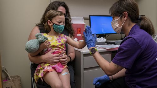 Nora Burlingame, 3, sits on the lap of her mother, Dina Burlingame, and gets a high five from nurse Luann Majeed after receiving her first dose of the Pfizer COVID-19 vaccination at UW Medical Center - Roosevelt on June 21, 2022, in Seattle. (David Ryder/Getty Images/TNS)