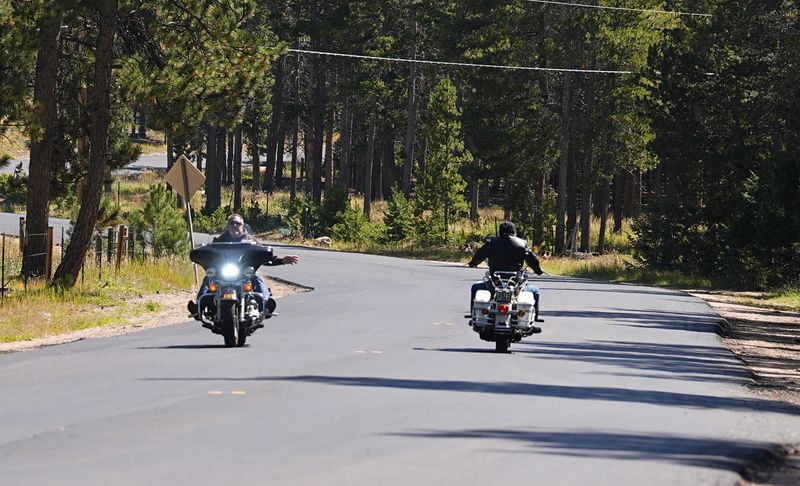 Motorcyclists gesture to each other as they pass in the 23000 block of Pleasant Park Road where a teenager, who was scouting for a location for lakeside homecoming photos, was shot in the face by a town councilman, Friday, Sept. 13, 2024, near Conifer, Colo. (AP Photo/David Zalubowski)