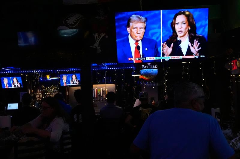 People watch TV screens showing a debate between Democratic presidential nominee Vice President Kamala Harris, right, and Republican presidential nominee former President Donald Trump, at Sports Grill Kendall, where the Miami-Dade Democratic Hispanic Caucus had organized a watch party, Tuesday, Sept. 10, 2024, in Miami. (AP Photo/Rebecca Blackwell)