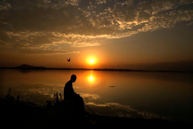 A Kashmiri man fishes as the sun sets over the Dal Lake on a hot summer day on the outskirts of Srinagar, Indian controlled Kashmir, Thursday, July 13, 2023. (AP Photo/Mukhtar Khan, File)