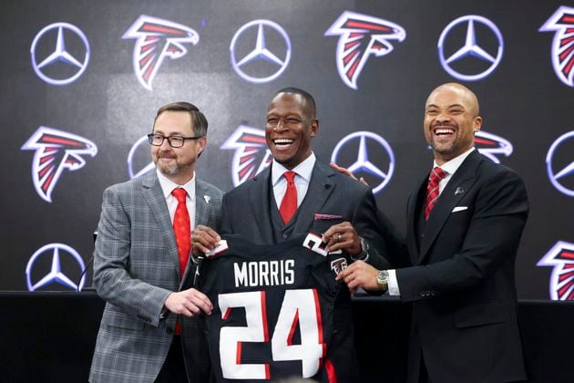 Atlanta Falcons new coach Raheem Morris poses with a Falcons jersey at Mercedes-Benz Stadium, Monday, February 5, 2024, in Atlanta. Also pictured is Falcons president Greg Beadles, left, and general manager Terry Fontenot. (Jason Getz / Jason.Getz@ajc.com)