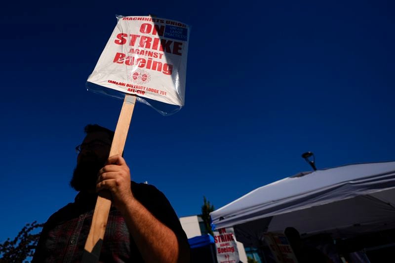 A Boeing worker waves a picket sign Tuesday, Sept. 24, 2024, as workers continue to strike outside the company's factory in Renton, Wash. (AP Photo/Lindsey Wasson)