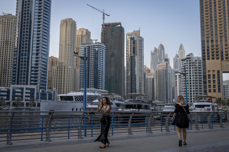 A woman takes a photograph as she walks along Dubai Marina Walk in Dubai, United Arab Emirates, Tuesday, Aug. 13, 2024. (AP Photo/Altaf Qadri)