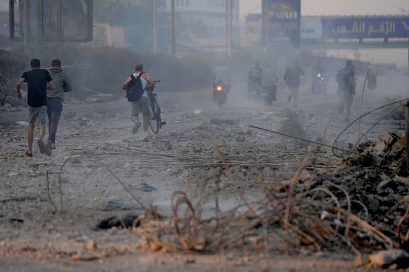 People run from a warplane sound on the debris of destroyed buildings hit by Israeli airstrikes in Dahiyeh, Beirut, Lebanon, Sunday, Oct. 6, 2024. (AP Photo/Hussein Malla)